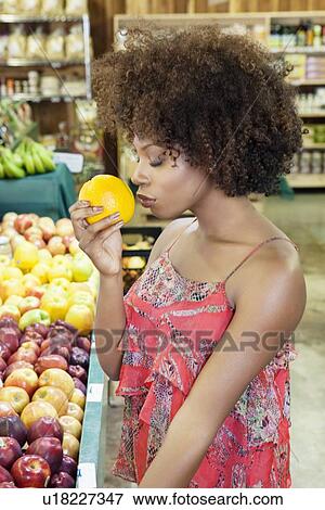 Side view of African American woman smelling fresh orange at supermarket View Large Photo Image Stock Photo - Side view of African American woman smelling fresh orange at supermarket. Fotosearch