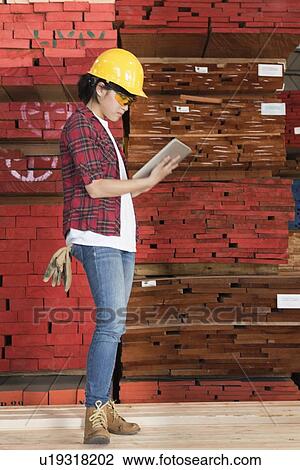 Side view of an Asian female industrial worker using tablet PC with stacked wooden planks in background View Large Photo Image Stock Image - Side view of an Asian female industrial worker using tablet PC with stacked wooden planks in background. Fotosearch