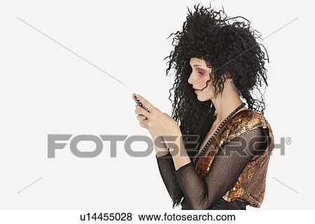 Stock Photo - Side view of young Goth woman with teased hair texting on mobile phone over gray background. Fotosearch