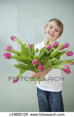 Smiling boy holding out tulip flowers against gray background View Large Photo Image Stock Photo - Smiling boy holding out tulip flowers against gray background. Fotosearch