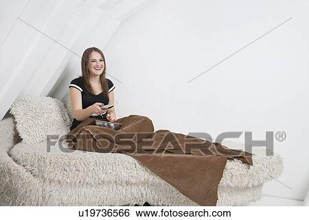 Smiling young woman in bed holding remote control View Large Photo Image Stock Photograph - Smiling young woman in bed holding remote control. Fotosearch
