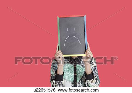 Stock Photograph - Teenage boy holding sad smiley face sign over pink background. Fotosearch