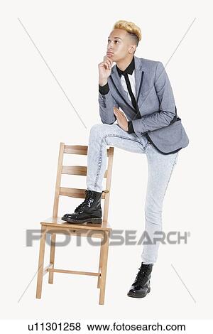 Stock Photo - Thoughtful teenage boy standing with one leg on chair over gray background. Fotosearch