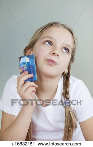 Stock Image - Thoughtful young girl holding credit card over gray background. Fotosearch