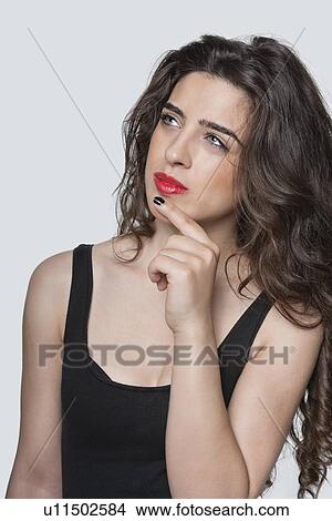 Thoughtful young woman looking away with hand on chin over gray background View Large Photo Image Picture - Thoughtful young woman looking away with hand on chin over gray background. Fotosearch