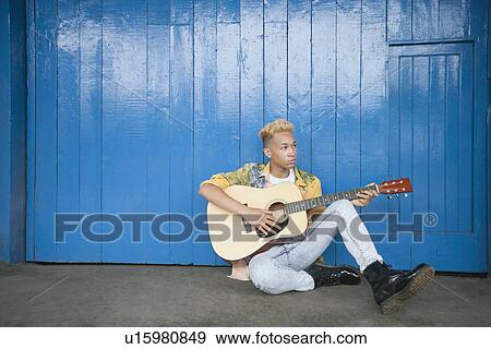 Trendy teenage boy playing guitar as he sits against wood paneled wall View Large Photo Image Stock Photo - Trendy teenage boy playing guitar as he sits against wood paneled wall. Fotosearch