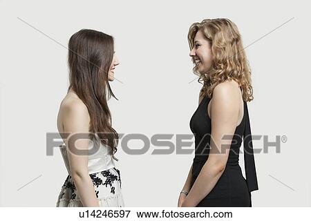 Two female friends looking at each other and smiling over gray background View Large Photo Image Stock Photo - Two female friends looking at each other and smiling over gray background. Fotosearch