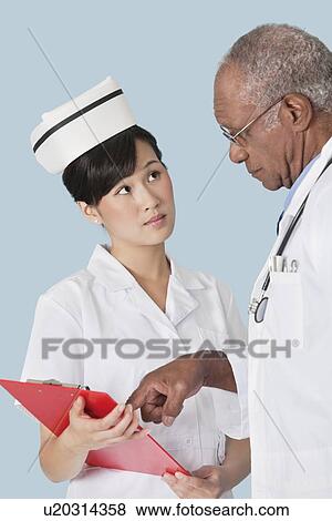 Stock Photo - Two medical professionals having a discussion over medical report against light blue background. Fotosearch