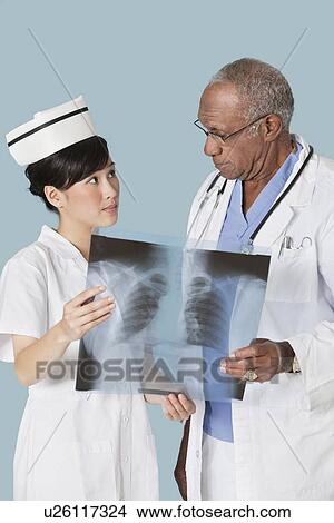 Two medical professionals holding x-ray report while looking at each other over light blue background View Large Photo Image Picture - Two medical professionals holding x-ray report while looking at each other over light blue background. Fotosearch