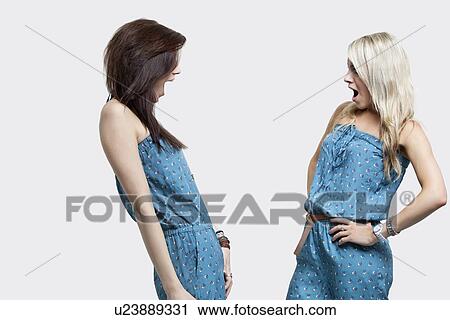 Two shocked women wearing matching jump suits looking at each other over gray background View Large Photo Image Stock Image - Two shocked women wearing matching jump suits looking at each other over gray background. Fotosearch