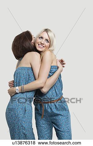 Two young female friends in matching jump suits hugging each other over gray background View Large Photo Image Stock Photo - Two young female friends in matching jump suits hugging each other over gray background. Fotosearch