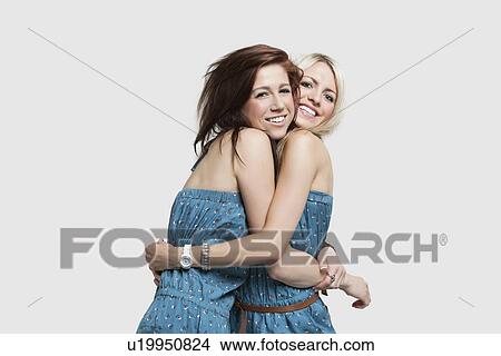 Two young women in matching jump suits embracing each other over gray background View Large Photo Image Picture - Two young women in matching jump suits embracing each other over gray background. Fotosearch