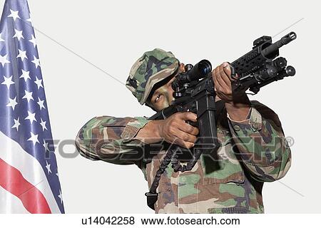 Stock Photo - US Marine Corps soldier aiming M4 assault rifle with American flag against gray background. Fotosearch