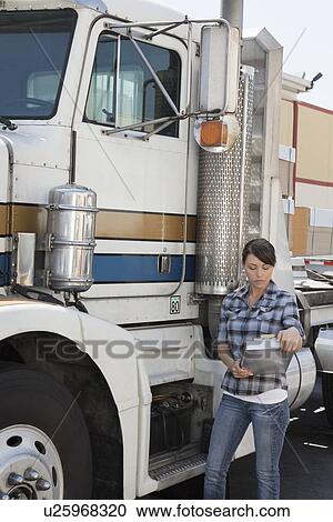 Stock Image - Woman looking at clipboard while standing by flatbed truck. Fotosearch