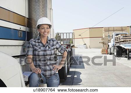 Picture - Woman looking away while standing by flatbed truck in timber yard. Fotosearch