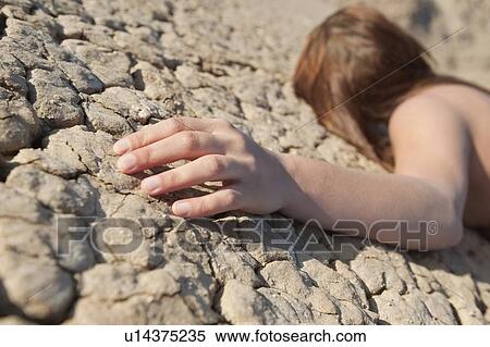 Stock Photography - Woman lying on cracked land with focus on hand. Fotosearch