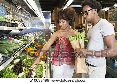 Stock Photo - Young African American couple buying green vegetables at supermarket. Fotosearch