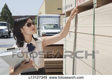Stock Photo - Young Asian woman inspecting wooden planks at timber yard. Fotosearch