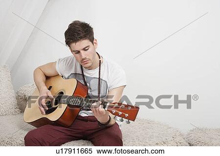 Young Caucasian man playing guitar while sitting on fur sofa View Large Photo Image Stock Photography - Young Caucasian man playing guitar while sitting on fur sofa. Fotosearch