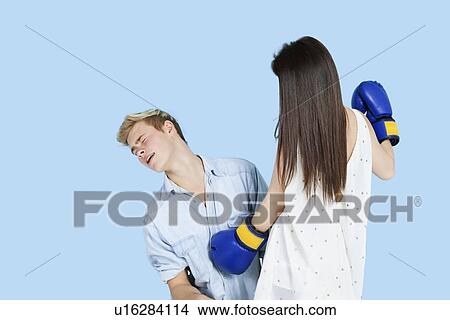 Picture - Young female boxer punching man over blue background. Fotosearch