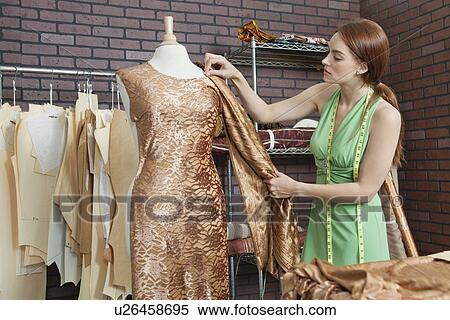 Stock Photography - Young female fashion designer matching cloth with fabric draped on tailor's dummy. Fotosearch