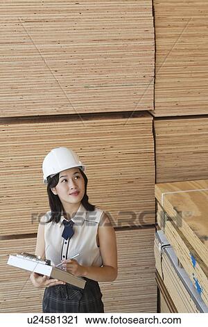 Stock Image - Young female industrial worker inspecting wooden planks. Fotosearch