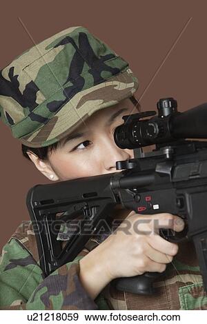 Stock Photo - Young female US Marine Corps soldier aiming M4 assault rifle over brown background. Fotosearch