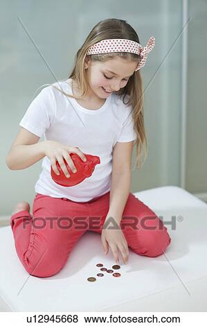 Stock Photo - Young girl with piggy bank counting coins on bed. Fotosearch