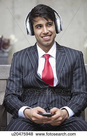 Stock Photo - Young Indian businessman listening music on headphones. Fotosearch