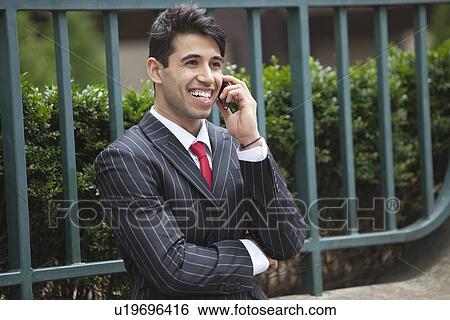 Young Indian businessman on call against fence View Large Photo Image Stock Photograph - Young Indian businessman on call against fence. Fotosearch
