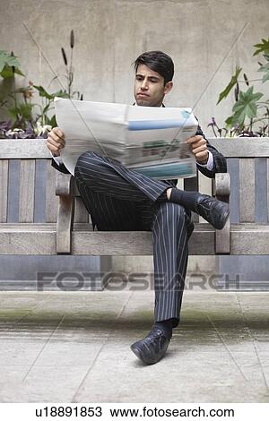 Young Indian businessman reading newspaper while sitting on bench View Large Photo Image Stock Image - Young Indian businessman reading newspaper while sitting on bench. Fotosearch