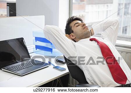 Stock Photograph - Young Indian businessman relaxing in chair at office. Fotosearch