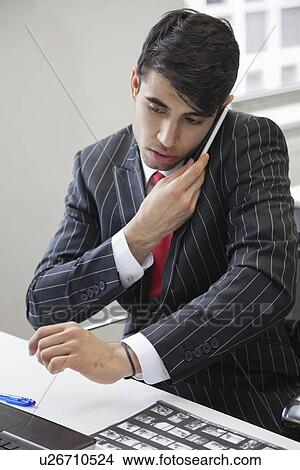 Young Indian businessman using cell phone at office desk View Large Photo Image Picture - Young Indian businessman using cell phone at office desk. Fotosearch