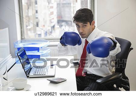 Young Indian businessman wearing boxing gloves at office desk View Large Photo Image Stock Image - Young Indian businessman wearing boxing gloves at office desk. Fotosearch