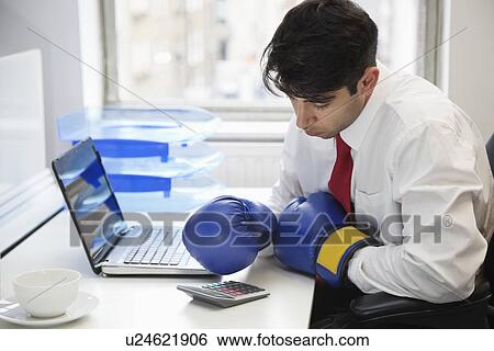Young Indian businessman wearing boxing gloves while using calculator at office desk View Large Photo Image Stock Photograph - Young Indian businessman wearing boxing gloves while using calculator at office desk. Fotosearch