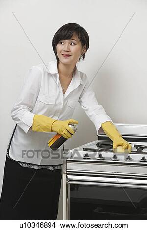Young maidservant looking away while cleaning stove against gray background View Large Photo Image Picture - Young maidservant looking away while cleaning stove against gray background. Fotosearch
