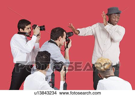 Picture - Young male celebrity shielding face from photographers over red background. Fotosearch