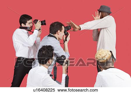 Young male celebrity shielding face from photographers over red background View Large Photo Image Stock Photography - Young male celebrity shielding face from photographers over red background. Fotosearch