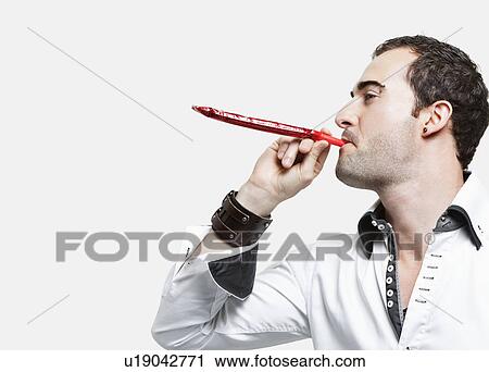 Young man blowing party blower against gray background View Large Photo Image Stock Image - Young man blowing party blower against gray background. Fotosearch