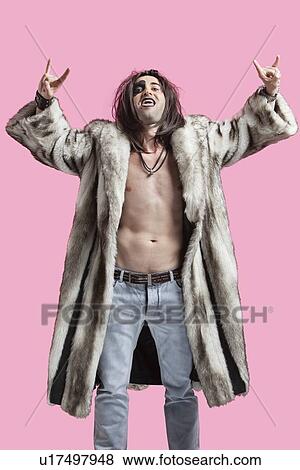Stock Photo - Young man in fur coat gesturing rock music sign over pink background. Fotosearch