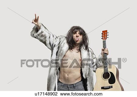 Stock Image - Young man in fur coat holding guitar while gesturing over gray background. Fotosearch
