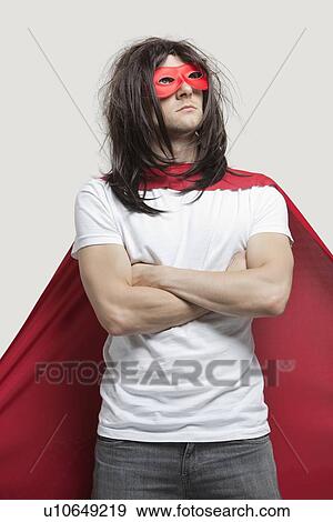 Young man in super hero costume standing with arms crossed against gray background View Large Photo Image Stock Photo - Young man in super hero costume standing with arms crossed against gray background. Fotosearch