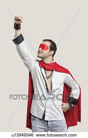 Young man in superhero costume with hand raised against gray background View Large Photo Image Stock Photograph - Young man in superhero costume with hand raised against gray background. Fotosearch
