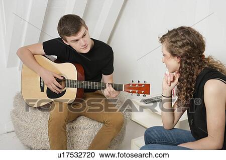 Young man strumming guitar besides female friend View Large Photo Image Stock Image - Young man strumming guitar besides female friend. Fotosearch