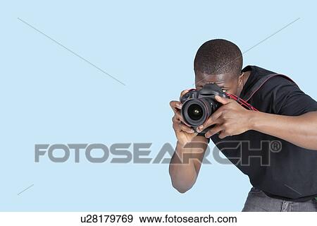 Stock Photo - Young man taking photo through digital camera over blue background. Fotosearch
