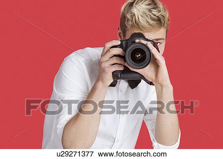 Young man taking picture with digital camera over red background View Large Photo Image Stock Photo - Young man taking picture with digital camera over red background. Fotosearch