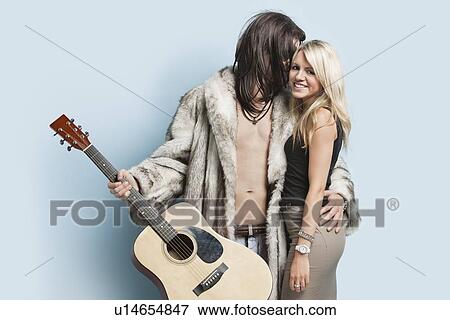 Young man with guitar embracing happy woman against light blue background View Large Photo Image Stock Photo - Young man with guitar embracing happy woman against light blue background. Fotosearch