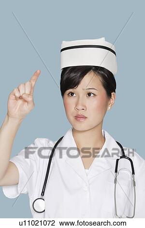 Stock Image - Young nurse using transparent screen over light blue background. Fotosearch
