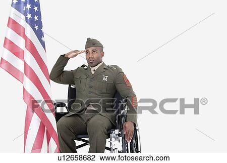 Stock Image - Young US soldier in wheelchair saluting American flag over gray background. Fotosearch