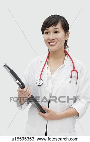 Stock Image - Young veterinarian holding report with stethoscope around neck over gray background. Fotosearch